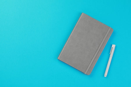 Gray notebook and pen on turquoise background, flat lay. Space for textの写真素材