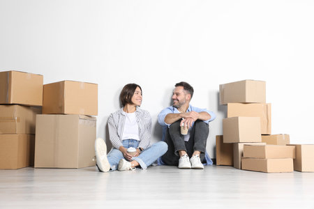 Happy couple with takeaway coffee resting on floor in new apartment. moving day