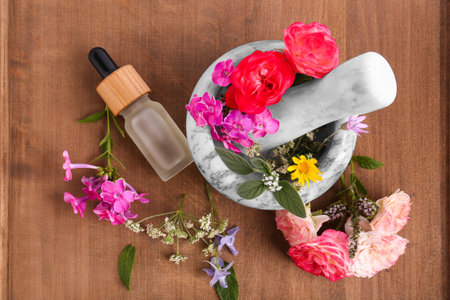 Bottle of essential oil, marble mortar and different flowers on wooden board, top viewの写真素材