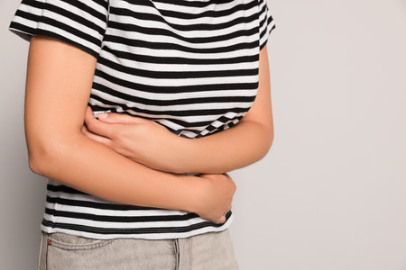 Young woman suffering from menstrual pain on gray background, closeup. Space for text