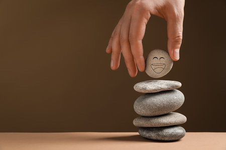 Closeup view of woman putting stone with drawn happy face on stack against dark beige background, space for text. Zen conceptの写真素材