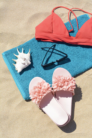 Towel, flip flops and bra on sand, above view. beach accessories