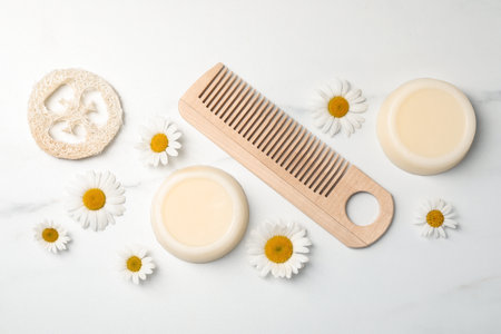Solid shampoo bars, comb and chamomiles on white marble table, flat lay. hair careの写真素材