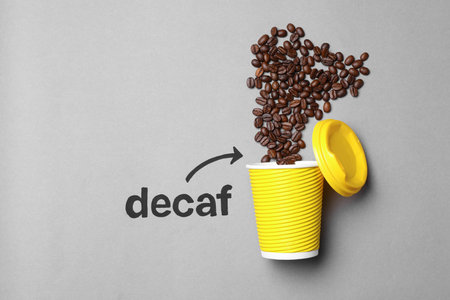 Word Decaf and arrow pointing at takeaway paper cup with coffee beans on light gray background, flat lay. Space for textの写真素材
