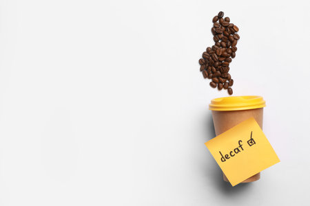 Note with word Decaf attached to takeaway cup and coffee beans on white background, flat lay. Space for textの写真素材
