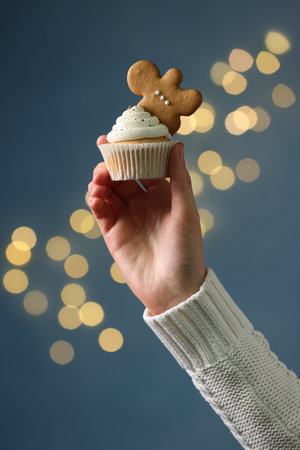 Woman holding tasty Christmas cupcake with gingerbread man cookie against blurred festive lights, closeupの写真素材