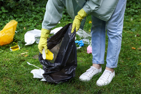Woman with plastic bag garbage collecting on green grass outdoors, closeupの写真素材
