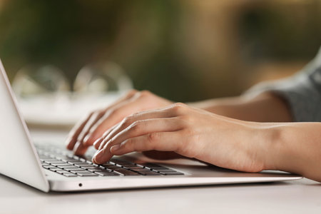 Woman working with laptop at white table indoors, closeup