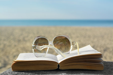 Book and sunglasses on table at seaside, space for textの写真素材