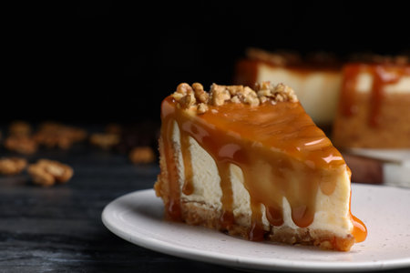Piece of delicious cake with caramel and walnuts on black marble table, space for text