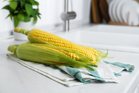 Tasty sweet corn cobs on white countertop in kitchen