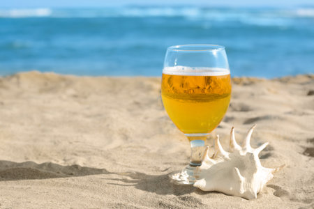 Glass of cold beer and seashell on sandy beach near sea. Space for textの写真素材