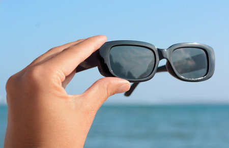 Woman holding stylish sunglasses near sea, closeupの写真素材