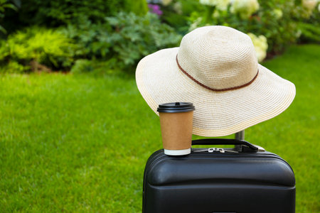Paper cup of hot coffee with beige hat on suitcase outdoors. Space for textの写真素材
