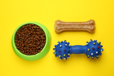 Pet toy, dog treat and bowl of food on yellow background, flat layの写真素材
