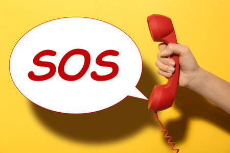 Woman holding telephone handset on yellow background, closeup. emergency SOS callの写真素材