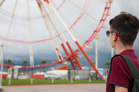 Teenage boy near large Ferris wheel outdoors. Space for textの写真素材