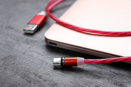 USB cable with type C connector and laptop on gray table, closeup