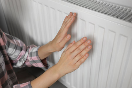 Woman warming hands on heating radiator near white wall, closeupの写真素材