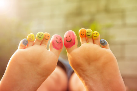 Teenage girl with smiling faces drawn on toes outdoors, closeupの写真素材