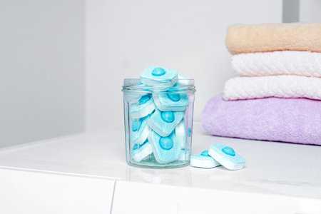 Jar with water softener tablets near stacked towels on washing machine