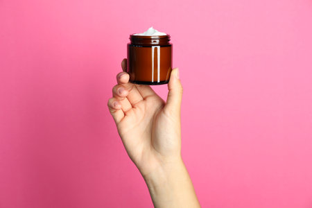Woman holding jar of face cream on pink background, closeupの写真素材