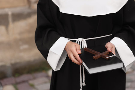 Young nun with Christian cross and Bible outdoors, closeup