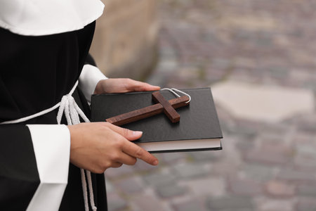 Young nun with Christian cross and Bible outdoors, closeup