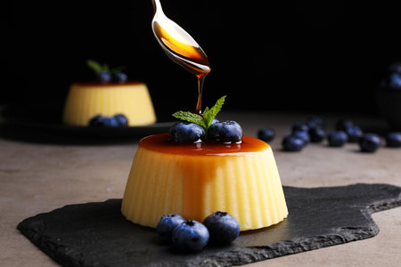 Pouring caramel onto delicious pudding with blueberries and mint on gray table against black background, closeupの写真素材