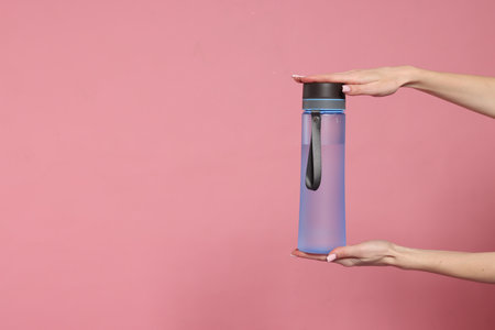 Woman holding transparent bottle on pink background, closeup. Space for text