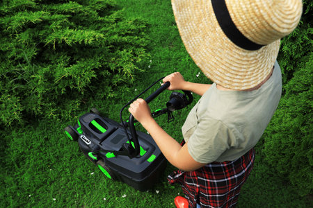 Woman cutting grass with lawn mower in garden