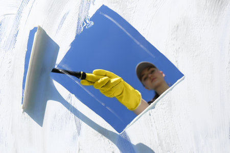 Woman cleaning glass with squeegee on sunny dayの写真素材