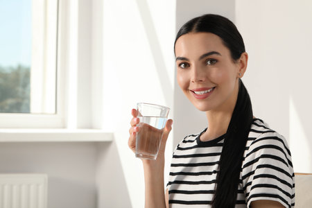 Young woman with glass of water indoors, space for text. Refreshing drinksの写真素材