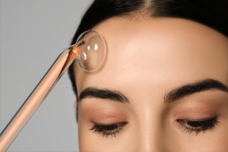 Woman using high frequency darsonval device on gray background, closeup