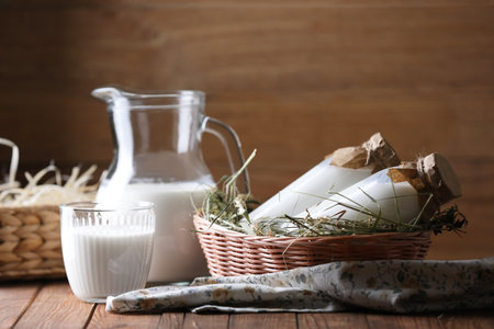 Tasty fresh milk in jug, bottles and glass on wooden tableの写真素材