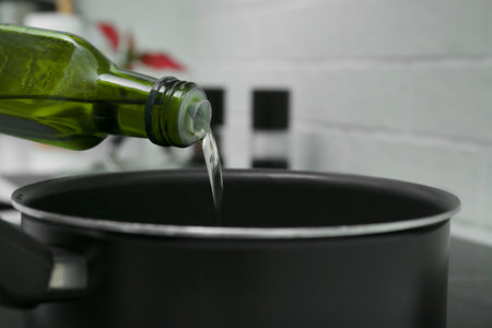 Pouring cooking oil from bottle into saucepan in kitchen, closeupの写真素材