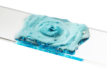Glass slide with turquoise facial gel on white background, closeup