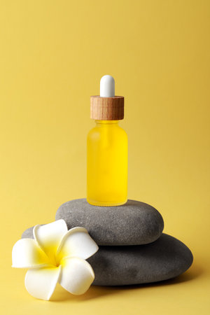 Bottle of face serum, spa stones and beautiful flower on yellow backgroundの写真素材
