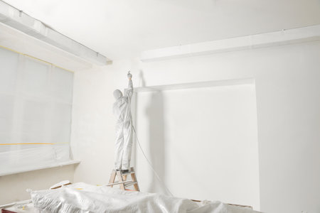 Decorator in protective overalls painting wall with spray gun indoorsの写真素材