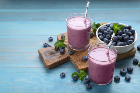 Glasses of blueberry smoothie with mint and fresh berries on turquoise wooden table. Space for textの写真素材