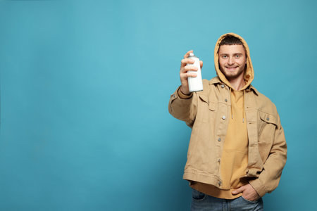 Handsome man holding white can of spray paint on light blue background. Space for textの写真素材