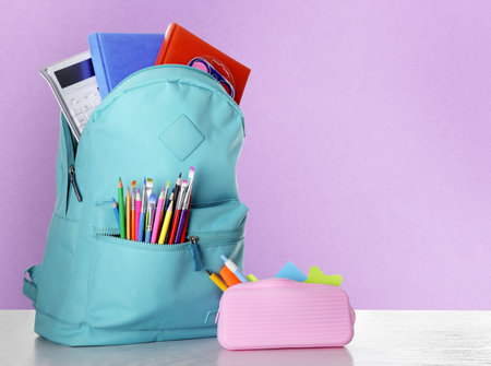 Backpack with school stationery on wooden table against violet background, space for textの写真素材