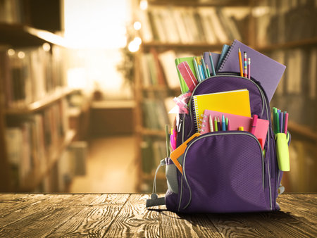 Backpack with school stationery on wooden table in library, space for textの写真素材