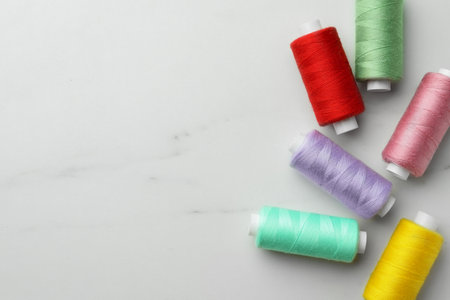Colorful sewing threads on white marble table, flat lay. Space for text