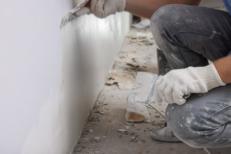 Worker plastering wall with putty knife indoors, closeupの写真素材
