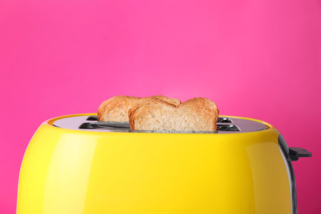 Yellow toaster with roasted bread against pink background, closeupの写真素材