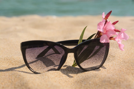 Beautiful sunglasses with flower on sand near the sea, closeupの写真素材