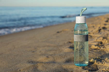 Glass bottle with water on wet sand near sea. Space for textの写真素材