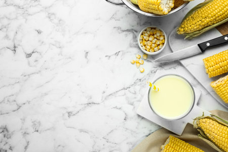 Tasty fresh corn milk in glass and cobs on marble table, flat lay. Space for text