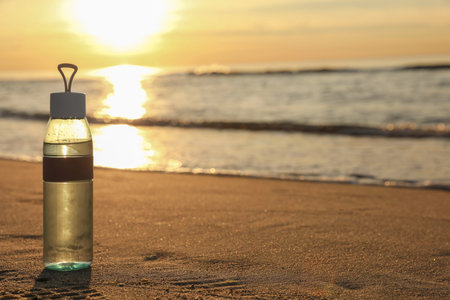 Glass bottle with water on wet sand near the sea at sunset. Space for textの写真素材